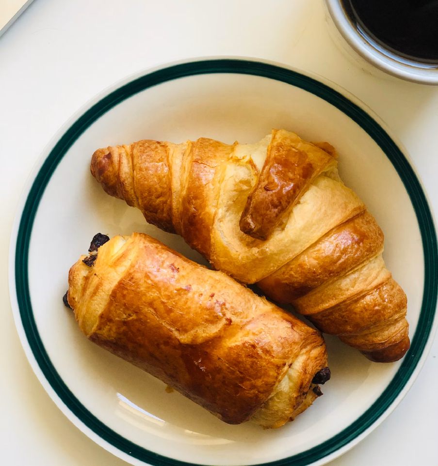 Golden croissants and pain au chocolat on a green-rimmed plate